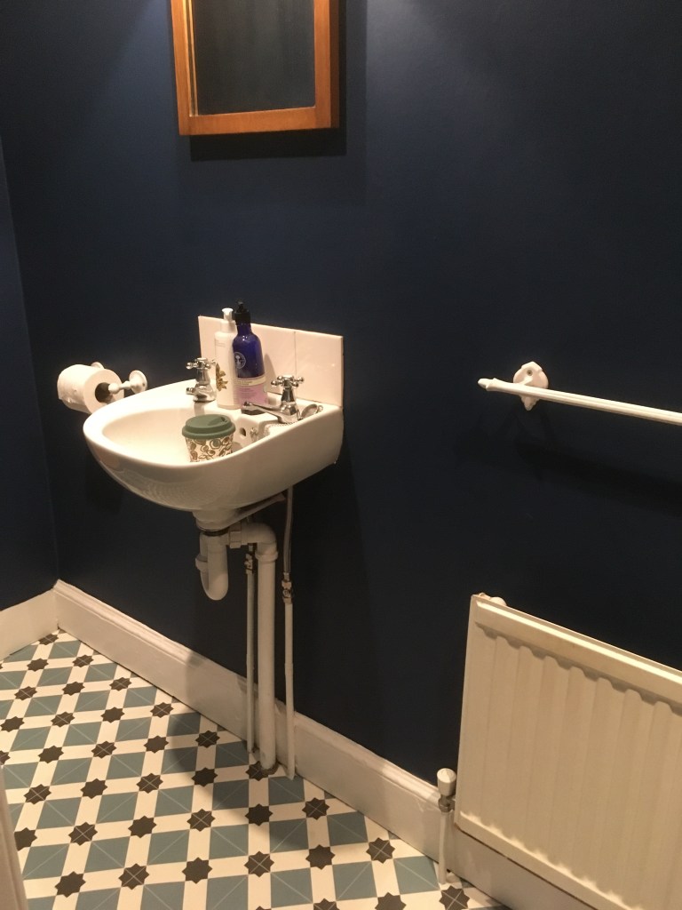 A newly painted bathroom - the bathroom sink, skirting board and radiator are a shiny bright white, whilst the walls of the bathroom are a dark blue.